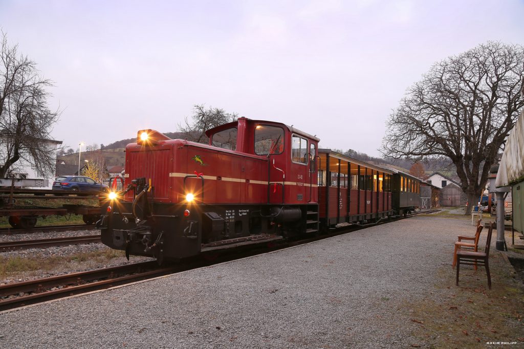 Lok V22.02 wartet mit ihrem Zug bestehend aus dem Sommerwagen 113 und dem Barwagen 371 im Bahnhof Dörzbach auf Abfahrt.